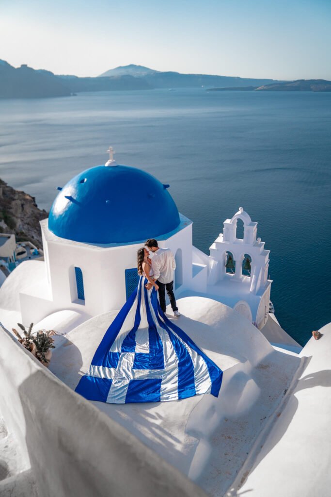 Danni and Fede on a rooftop in Santorini, Greece with a Greek flag flying dress